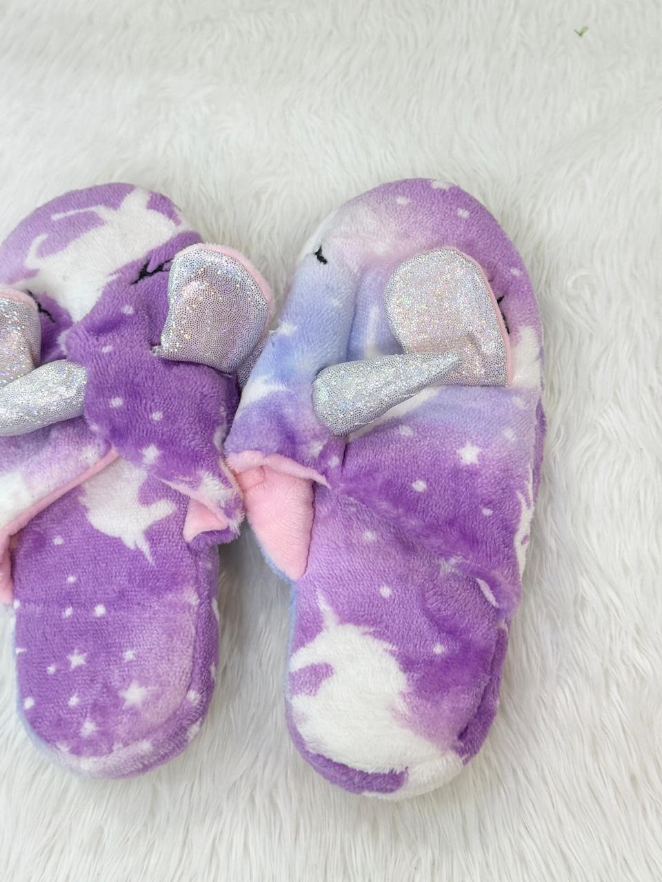 Pair of purple slippers with unicorn and star patterns on a white background