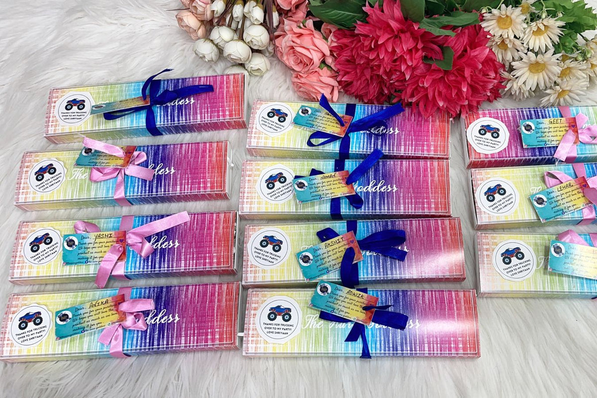 Twelve packaged horsebit gifts arranged in a grid on a white faux fur surface, decorated with pink, blue, and purple ribbons and colorful rainbow gradient wrapping paper. Pink and white flowers are arranged in the background.