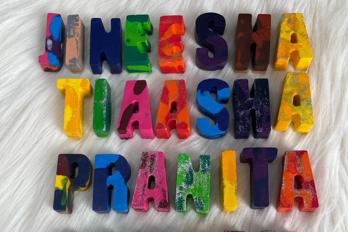 Custom colorful crayon name blocks spelling out 'JINESHA TIAASHA PRAHITA' arranged in three rows on a white faux fur background.